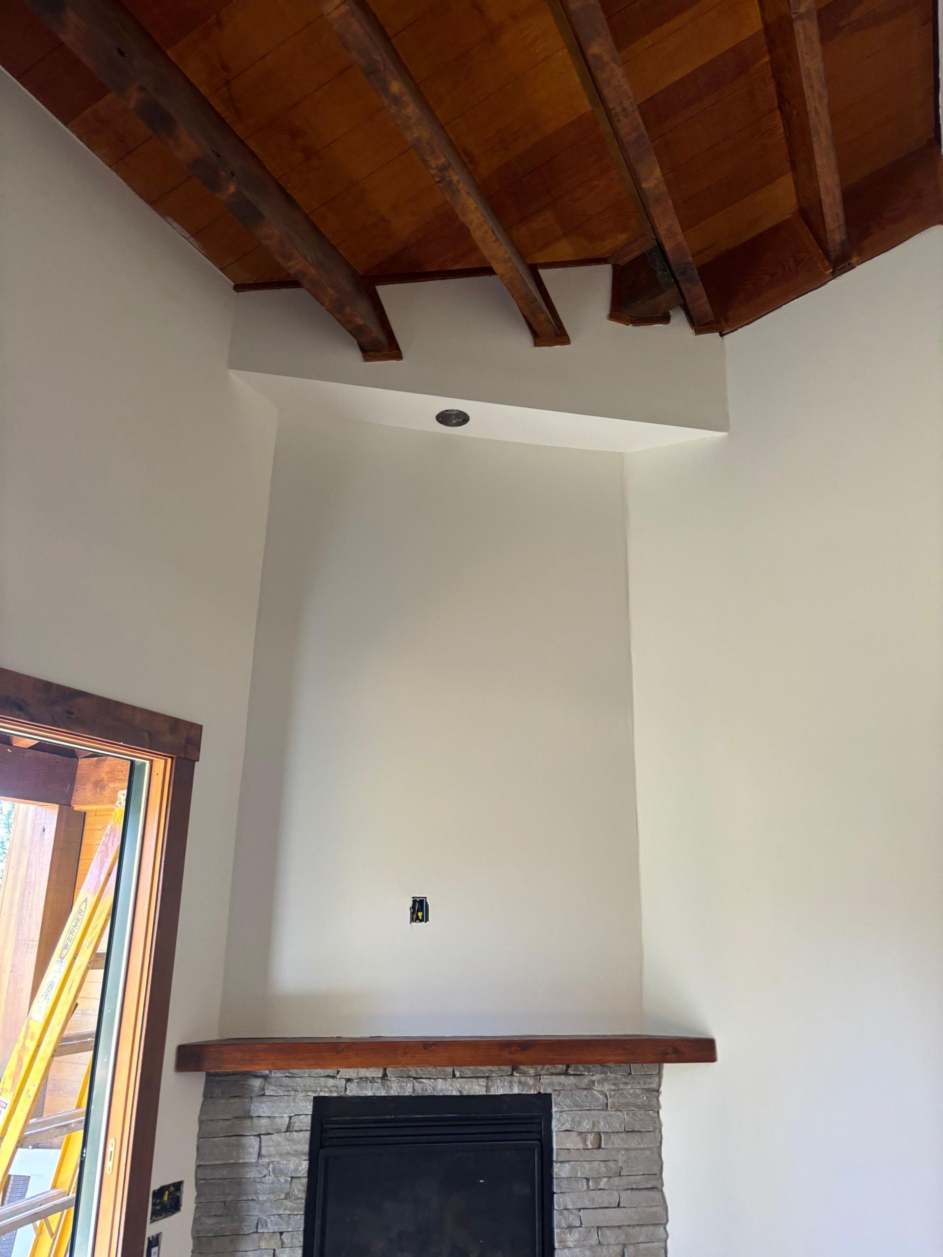 Interior with a stained timber beam ceiling above freshly painted walls and a stone fireplace