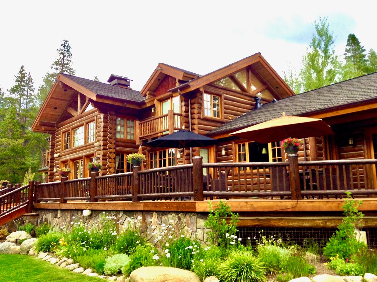 A large log home with freshly restained logs, deck rails and stone foundation